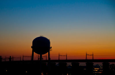 Low angle view of water tower on field against orange sky