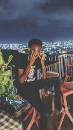 Full length of man sitting at illuminated restaurant against sky at night