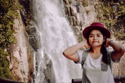 Portrait of beautiful young woman standing on rock against waterfall