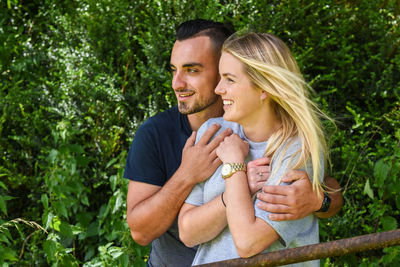 Happy young couple looking away while standing by railing at park