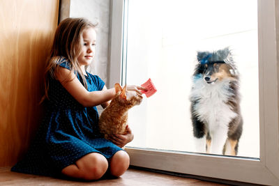 Cute girl sitting by door with cat and dog