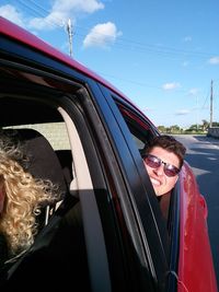 Portrait of happy young woman on car against sky