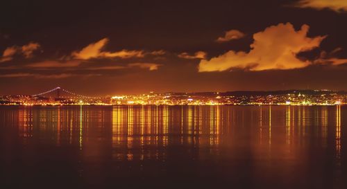 Illuminated cityscape by sea against sky at night