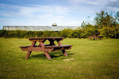 Empty bench on table by field against sky