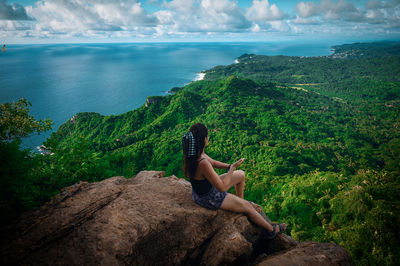 Woman on top of rock  by tropical jungle against sky