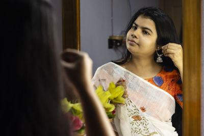 A beautiful indian woman in white saree wearing silver earrings in front of mirror with smiling face