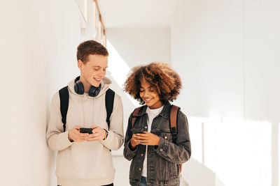 Happy friends using smartphone in corridor