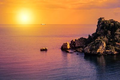 Scenic view of sea and rocks against sky during sunset