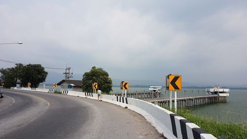 Road sign by street against sky in city