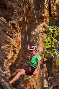 From below side view unrecognizable active fit senior man climbing on rocky cliff