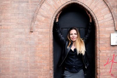 Portrait of young woman standing against brick wall