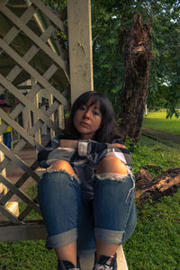 Portrait of woman sitting against built structure in park