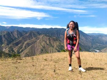 Full length of smiling young woman standing on mountain against sky