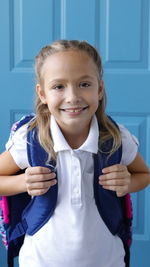 Portrait of a smiling girl standing against blue wall