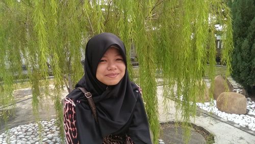 Portrait of girl wearing hijab while sitting by branches