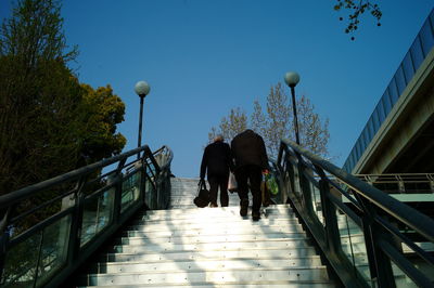 Rear view of people walking on footbridge against sky