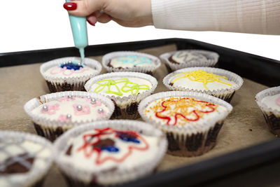 A woman squeezes colored frosting from a tube onto chocolate brown cupcakes covered white frosting.