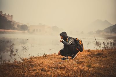 Man standing on field by lake against sky