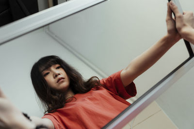 Close-up of young woman holding mirror standing against white background