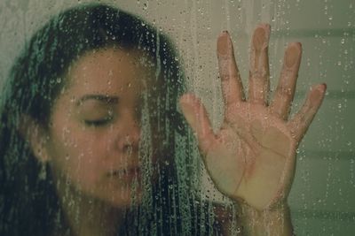 Close-up of woman with eyes closed seen through wet window