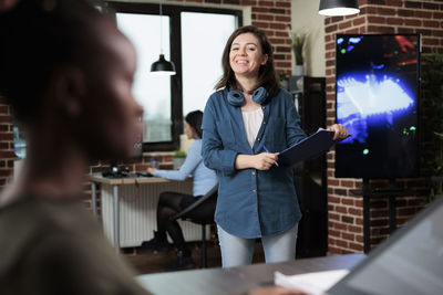 Portrait of young woman with clipboard standing in office