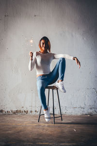 Full length of young woman sitting on chair against wall