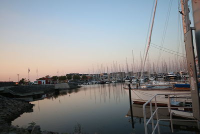 Sailboats moored in harbor at sunset