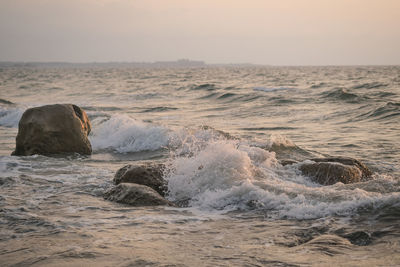 Waves splashing on rocks at shore against sky