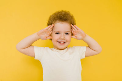 Happy surprised boy smiles and holds his hands on his head on a yellow background