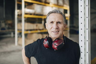 Portrait of smiling senior worker leaning on rack at industry