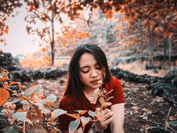 Young woman looking away while standing on tree during autumn