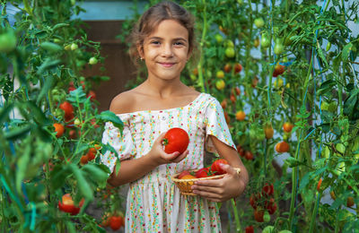 Portrait of smiling girl holding tomato at farm-