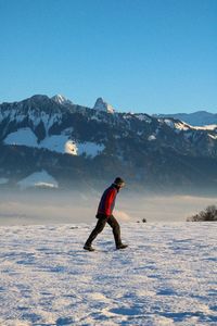 Full length of man walking on snowy field against snowcapped mountains