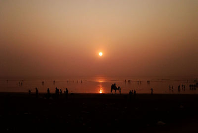 Silhouette people on beach against clear sky during sunset