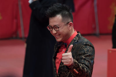 Young man wearing eyeglasses standing against red wall