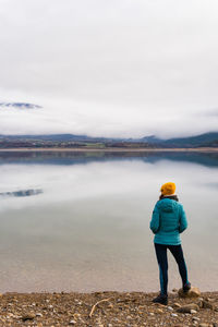 Unrecognizable woman wearing a jacket looking the fog on the mountain in the other side of the lake