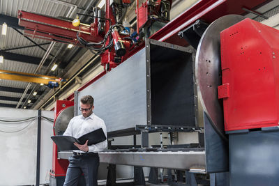 Businessman with folder standing on factory shop floor