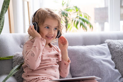 Cute girl listening music while sitting on sofa at home