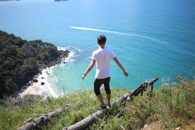 Rear view of woman standing on rock by sea