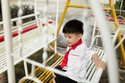 Cute boy playing while sitting on swing outdoors