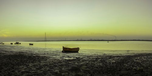 Boat moored on beach against sky during sunset