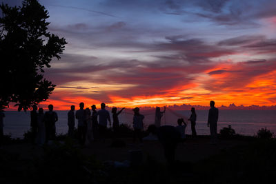 Silhouette people on land against sky during sunset