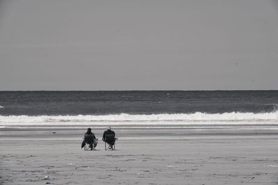 Men walking on beach against clear sky