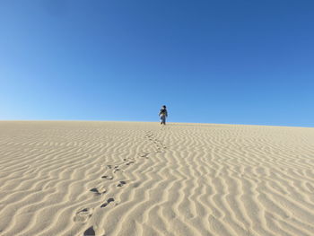 Rear view of man standing on sand dune against clear blue sky