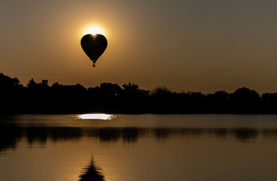 Silhouette hot air balloon in lake against sky during sunset