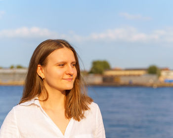 Pretty young girl standing by river on city embankment is enjoying summer