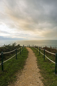 Wooden posts on footpath by sea against sky