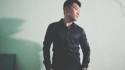 Young man looking away while standing against wall