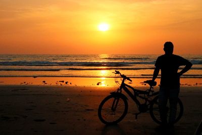 Silhouette man with bicycle standing at beach against sky during sunset