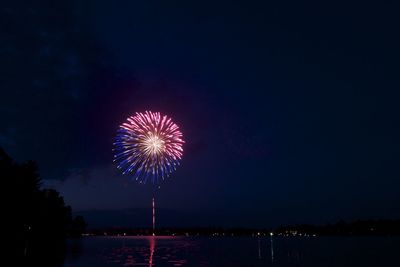 Low angle view of firework display over river against sky at night
